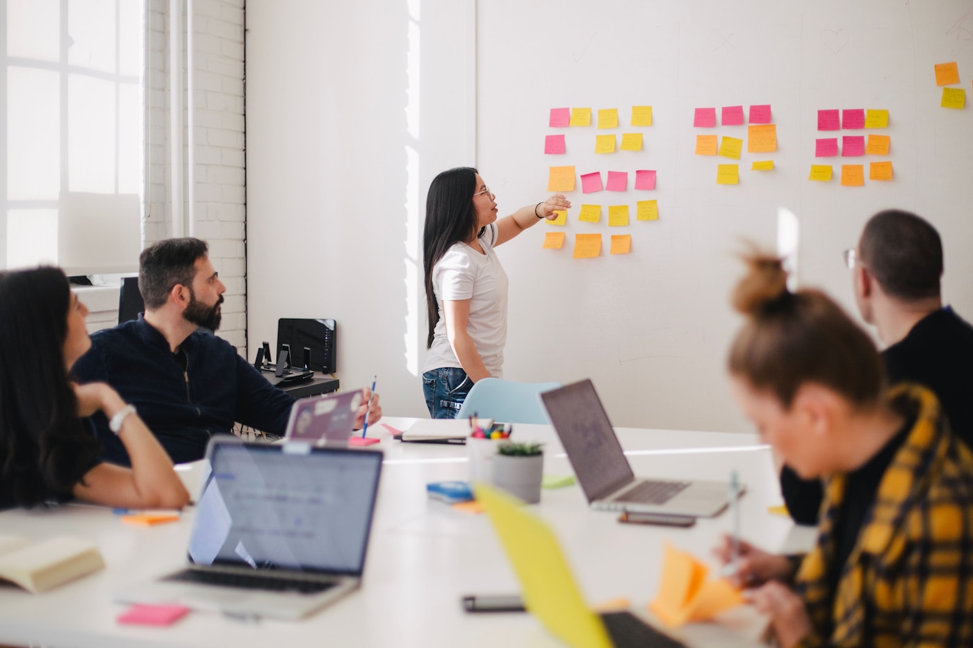 A colleague pointing at sticky notes on a wall during a meeting