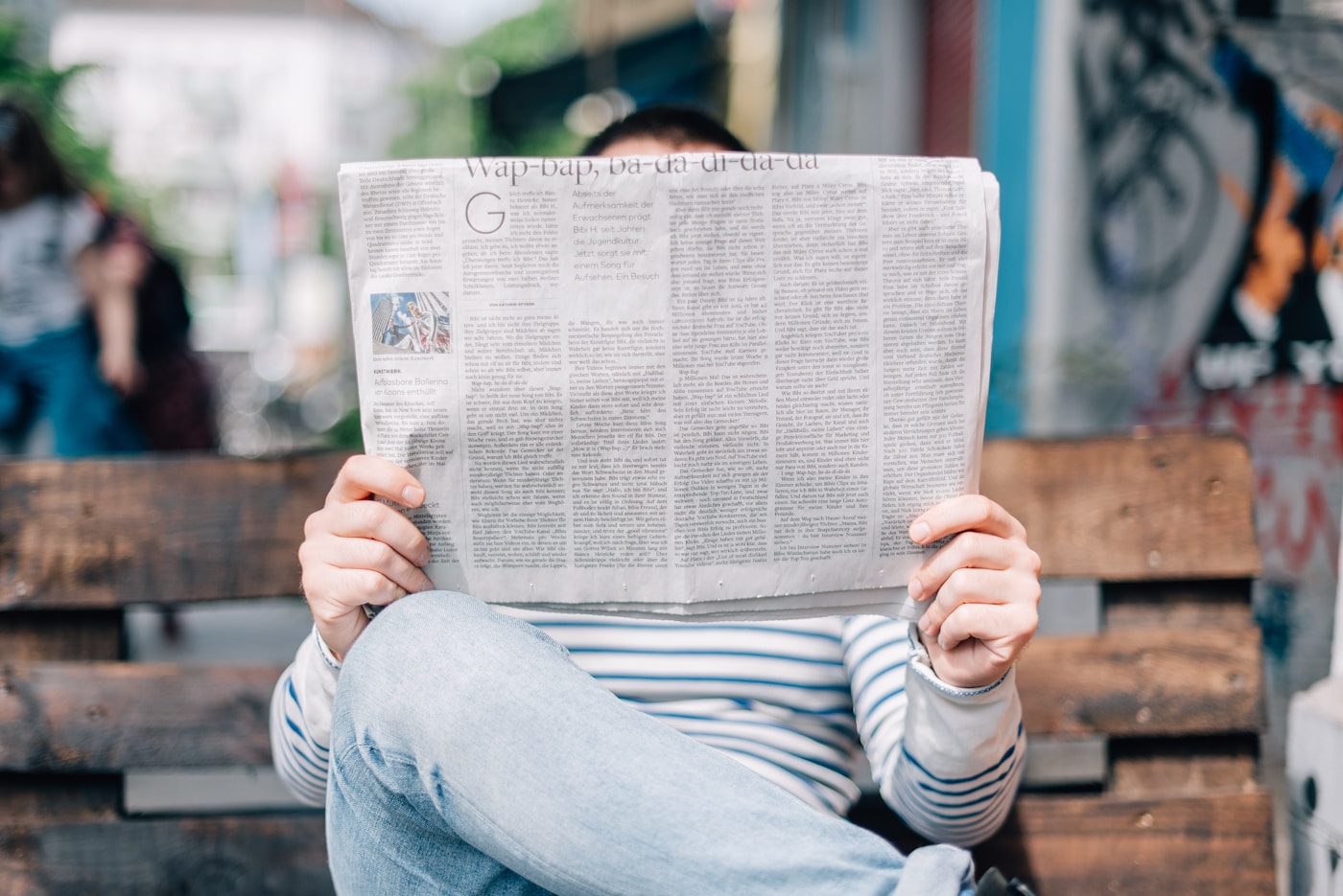 A person reading an open newspaper on an outdoor bench